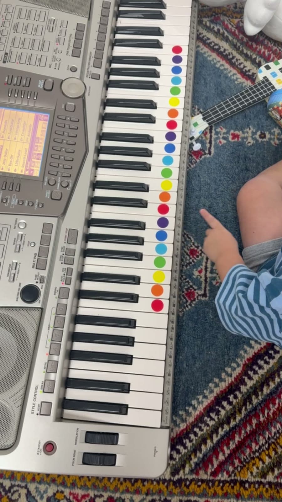 Un teclado con calcomanías de colores visto desde arriba, un bracito alcanza una tecla